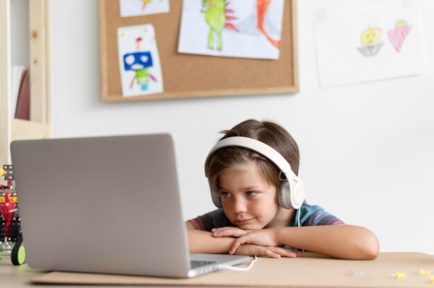 Medium shot kid sitting at desk with laptop