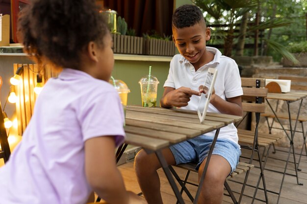 Medium shot kids sitting at table with tablet