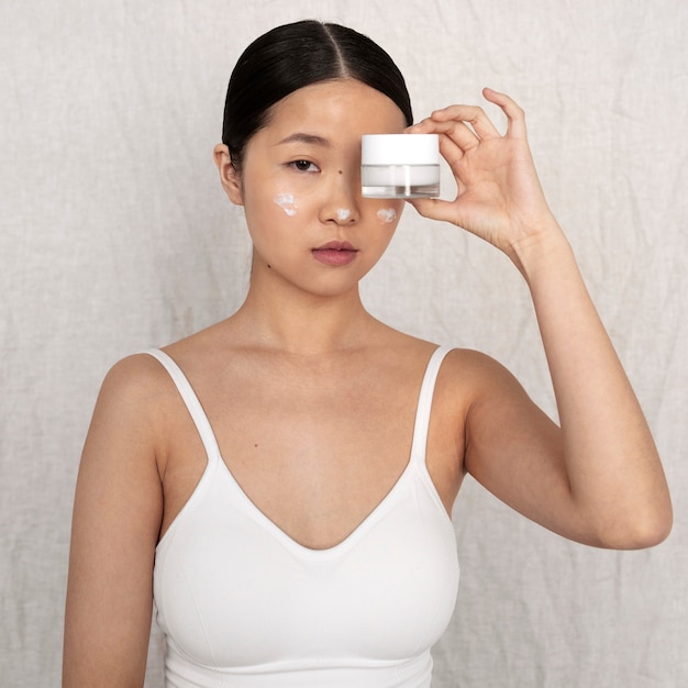 Free photo medium shot korean woman posing with face cream