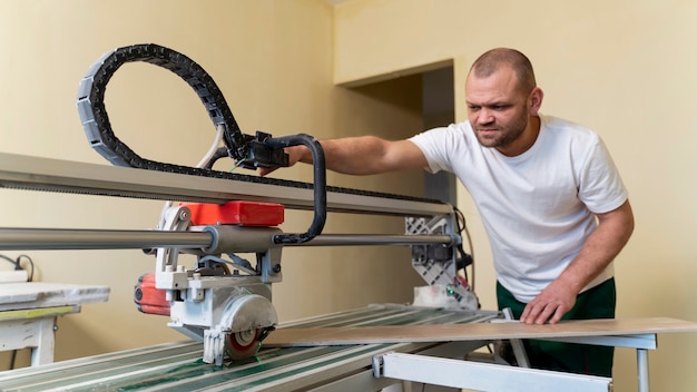 Medium shot man cutting tile with machine