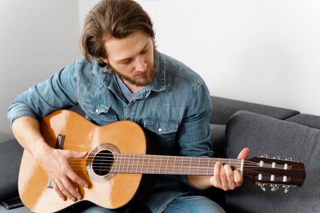 Medium shot man playing guitar on couch