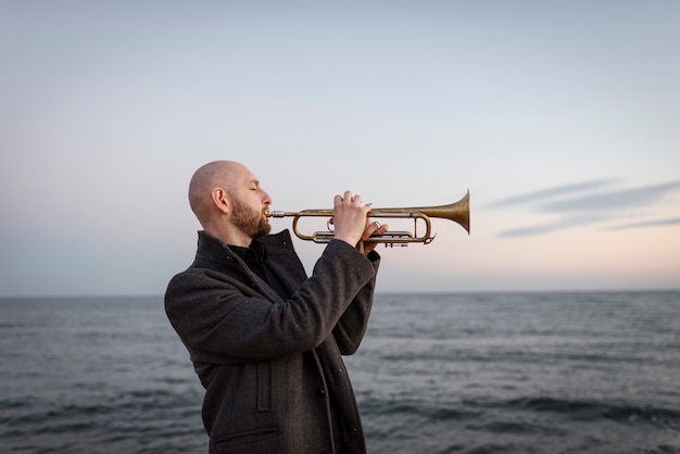 Free photo medium shot man playing trumpet at seaside