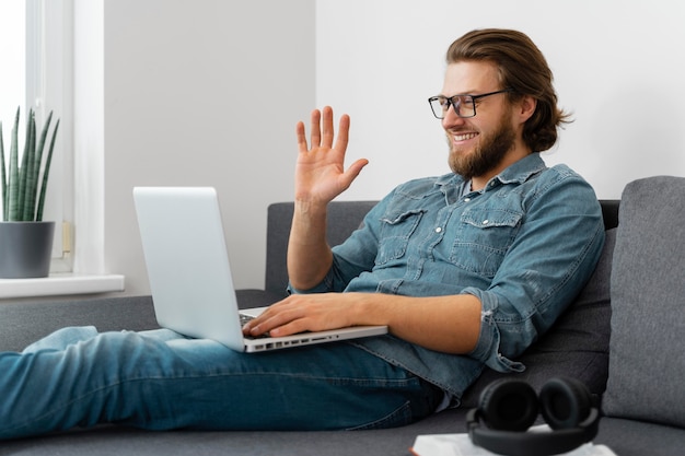 Medium shot man waving at laptop