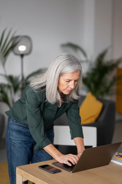 Medium shot old woman working on laptop at home