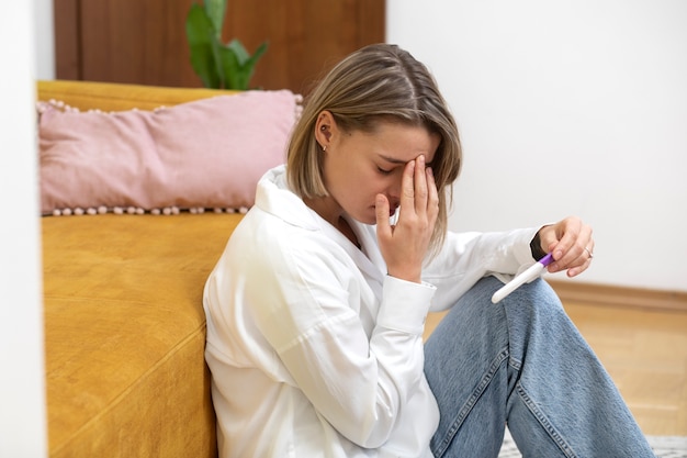 Free photo medium shot sad woman holding pregnancy test