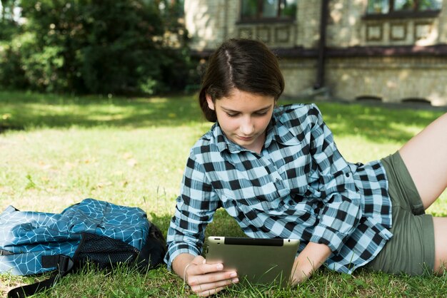 Medium shot of school girl using tablet sitting on lawn