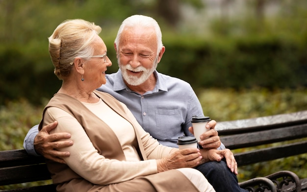 Medium shot senior couple on bench with cups