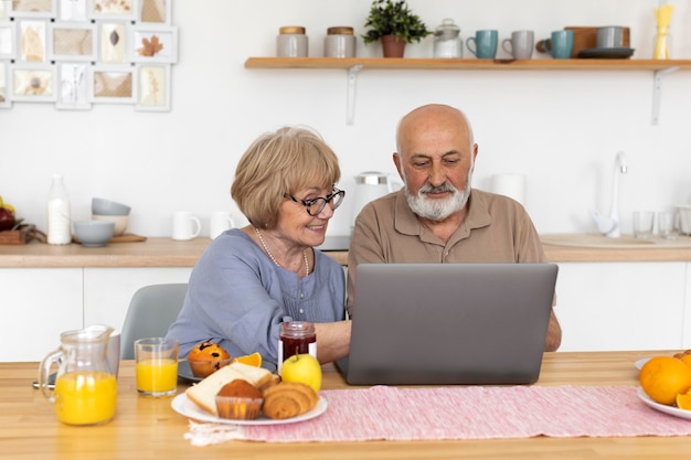 Medium shot senior couple sitting with laptop