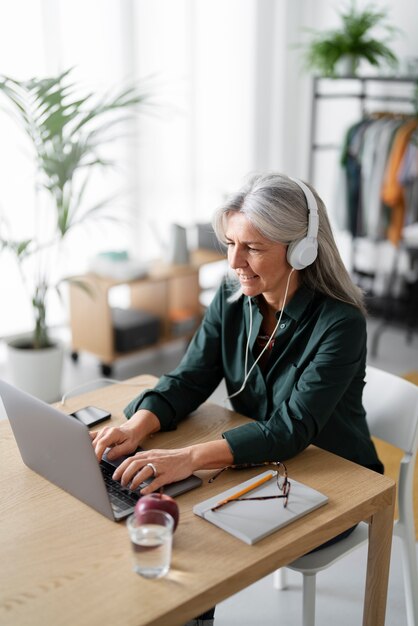 Medium shot senior woman with headphones at desk