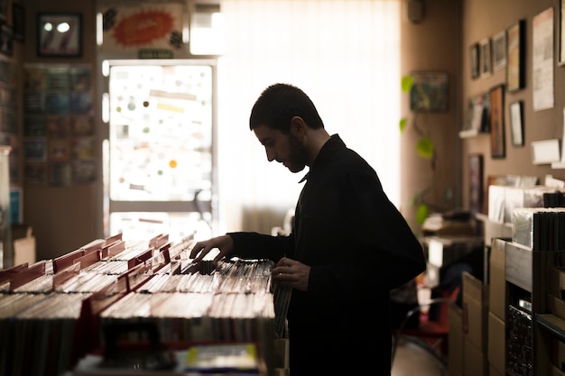 Medium shot side view of young man looking for vinyls in store