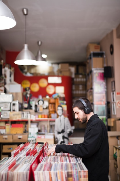 Free Photo medium shot side view of young man looking for vinyls in store