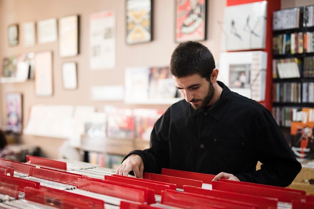 Medium shot side view of young man looking for vinyls in store