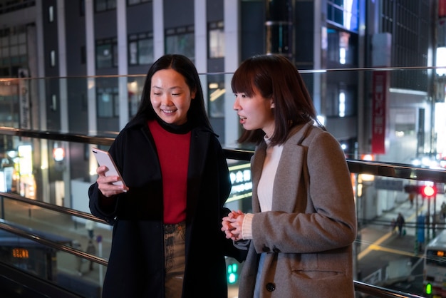 Free photo medium shot smiley girls with phone nighttime