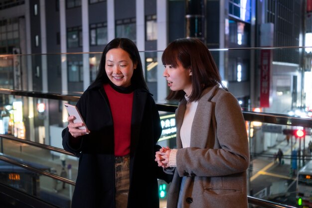 Medium shot smiley girls with phone nighttime