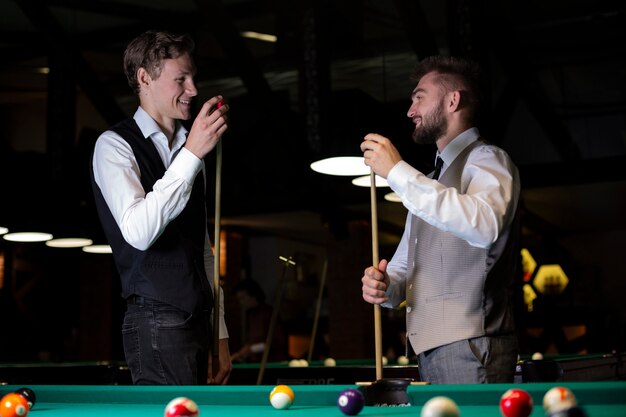 Medium shot smiley men with pool cues 