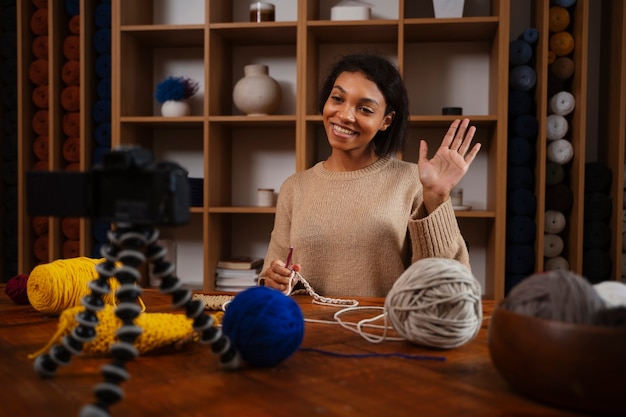 Medium shot smiley woman knitting on camera