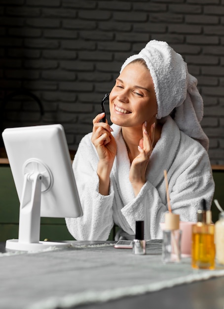 Medium shot smiley woman using facial tool