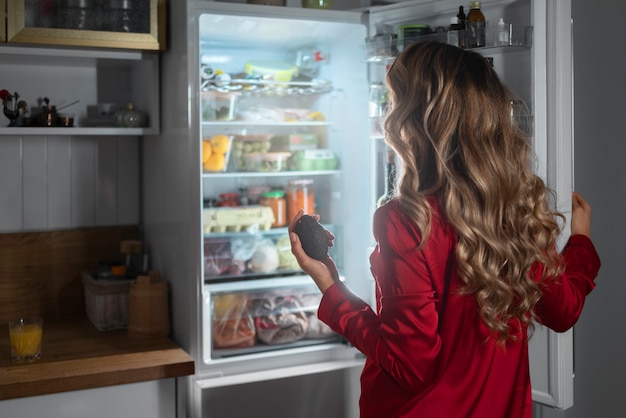 Free photo medium shot woman checking fridge at night