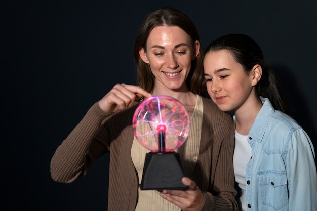 Free photo medium shot woman and girl interacting with a plasma ball