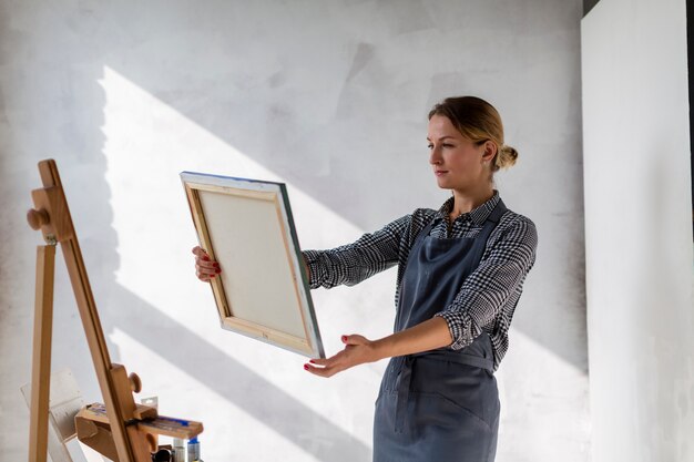 Medium shot of woman holding canvas in studio