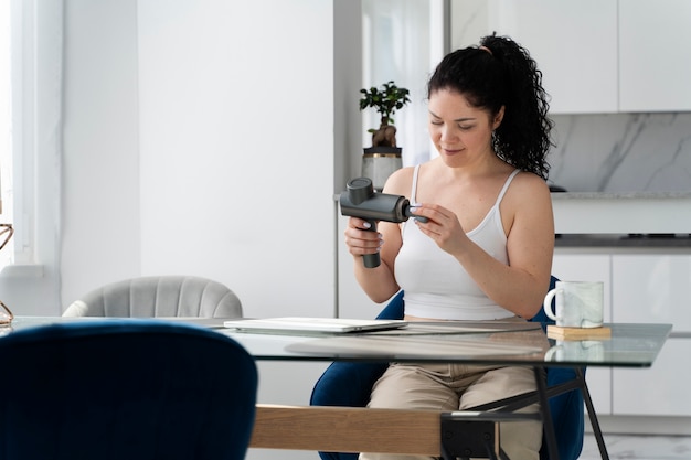 Medium shot woman using massage gun