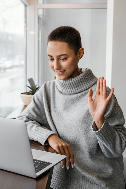 Medium shot woman waving at laptop