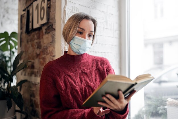 Medium shot woman with mask reading indoors