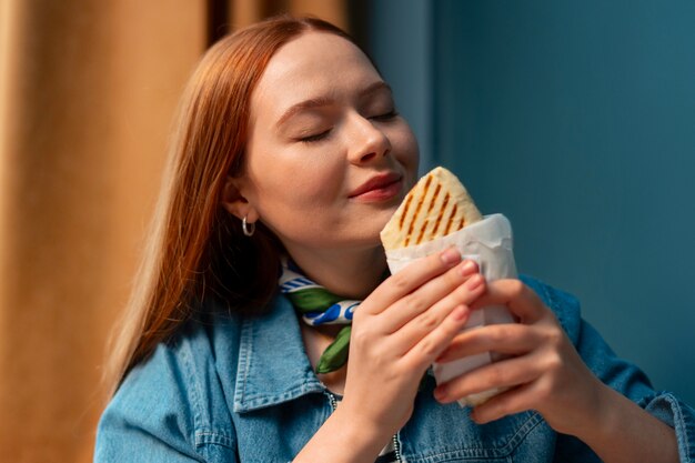 Medium shot woman with  paper-wrapped sandwich