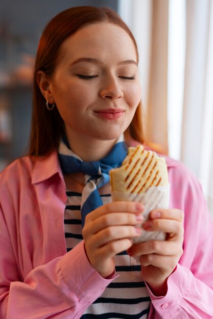 Medium shot woman with  paper-wrapped sandwich