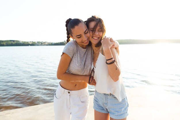 Medium shot women hugging next to a lake