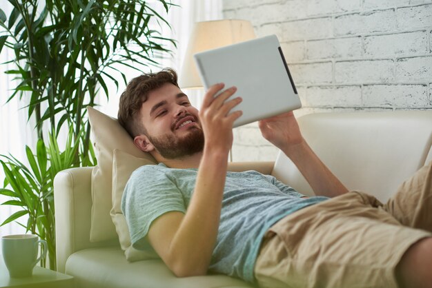 Medium shot of young man spending his leisure time reading ebook on his digital tablet