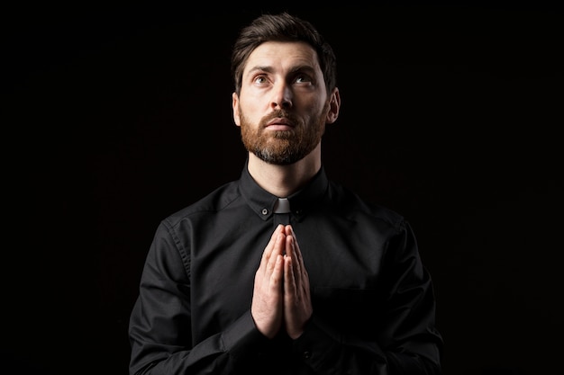 Medium shot young priest praying with dark background