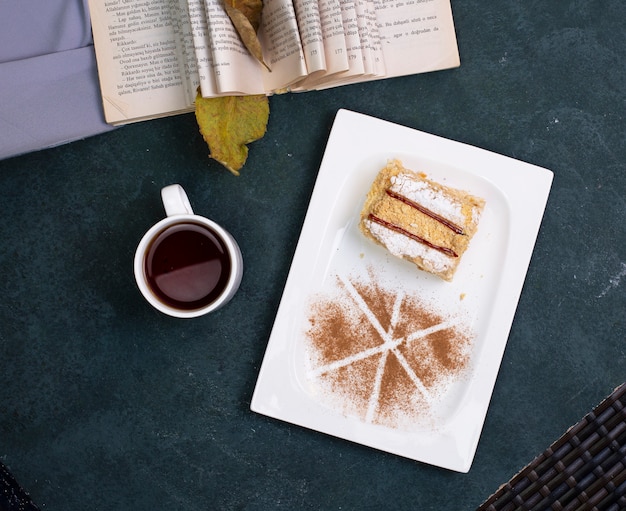 Free photo medovik cake with cocoa powder and a cup of tea on the stone table. top view.