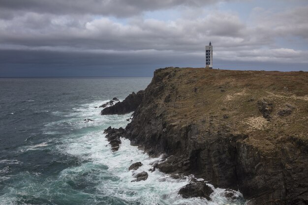 Meiras lighthouse on the Valdovino cliffs surrounded by the sea under a cloudy sky in Galicia, Spain