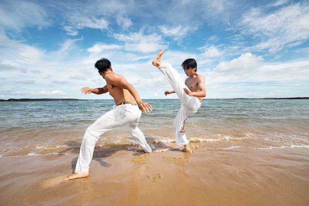 Free photo men by the beach practicing capoeira together