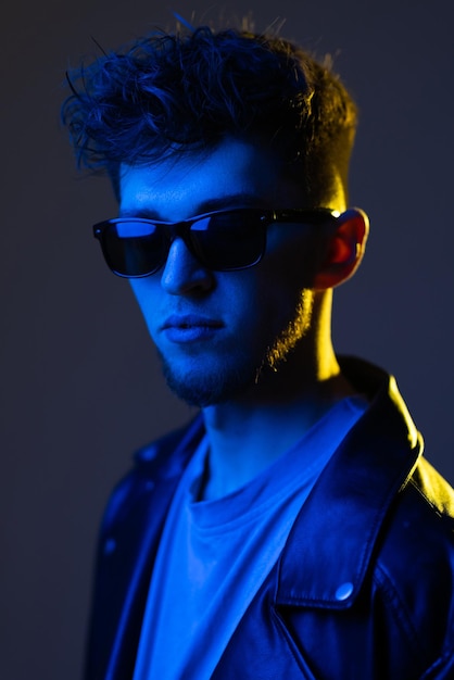 Men's Fashion Portrait Of Confident Handsome African American Guy In Stylish Leather Jacket And Sunglasses Posing Under Neon Lighting Over Purple Studio Background