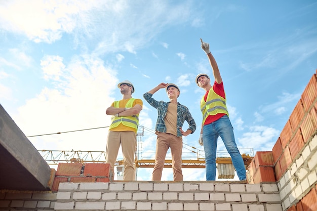 Men standing on brick wall of building under construction