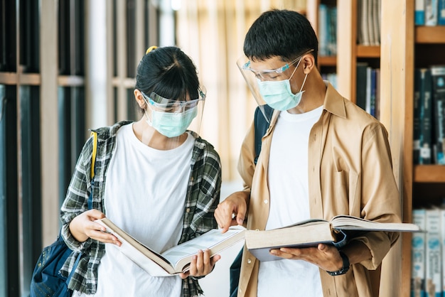 Men and women wearing masks stand and read in the library.