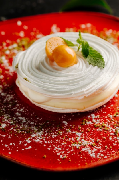 Free photo meringue cake with whipping cream and citrus fruit on the top in a red plate.