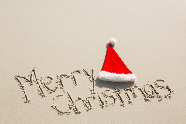 Free photo merry christmas written on sand with santa hat