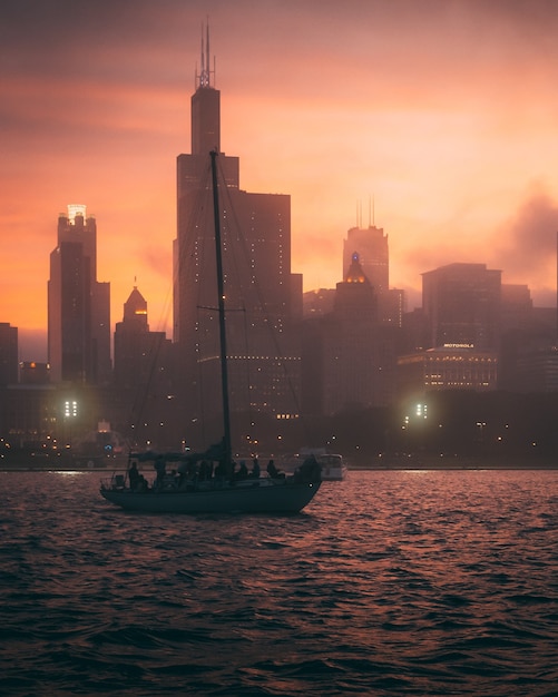 Free photo mesmerizing view of the boat in the ocean and the silhouettes of high buildings during sunset