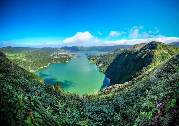 Mesmerizing view of the lake surrounded by mountains covered in green under the blue sky