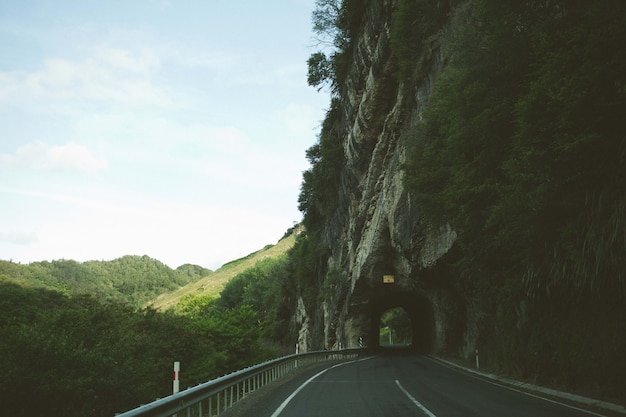 Mesmerizing view of the road through the rock cliff arch surrounded by trees and mountains