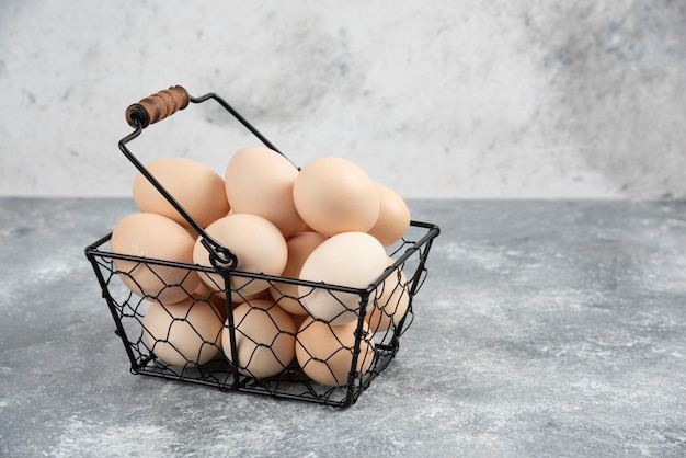 Metal basket of fresh organic raw eggs on marble surface.