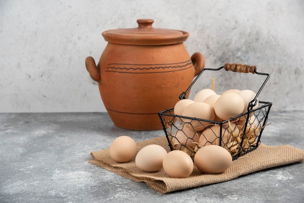 Metal basket of raw chicken eggs and antique vase on marble surface.