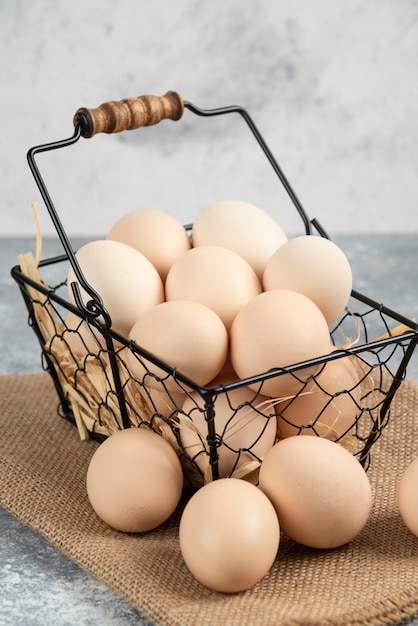 Metal basket of raw chicken eggs on marble surface.