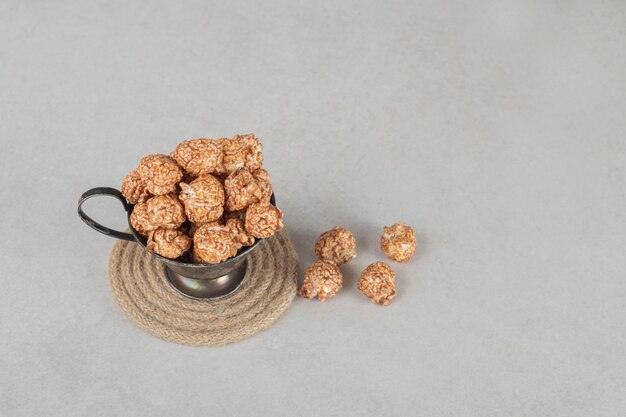 Metal cup overflowing with brown candied popcorn on marble.