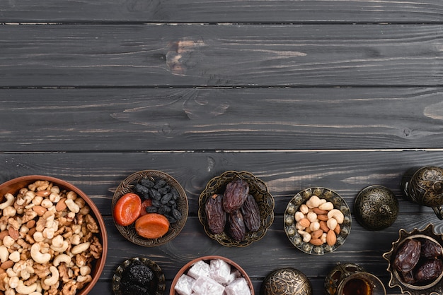 Free photo metallic bowl with sweet lukum; dried fruits and nuts on black wooden desk for ramadan