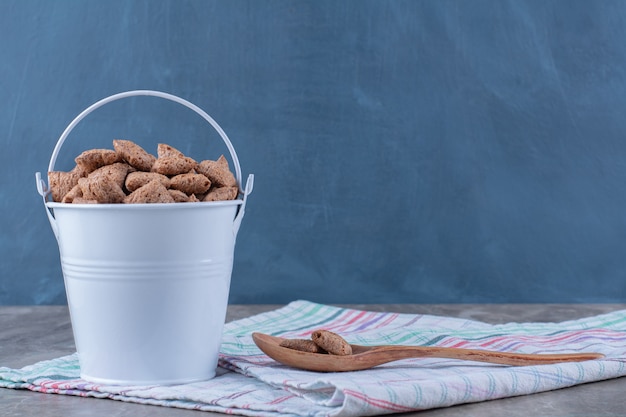 Free Photo a metallic bucket full of healthy chocolate pads corn flakes with a wooden spoon. 