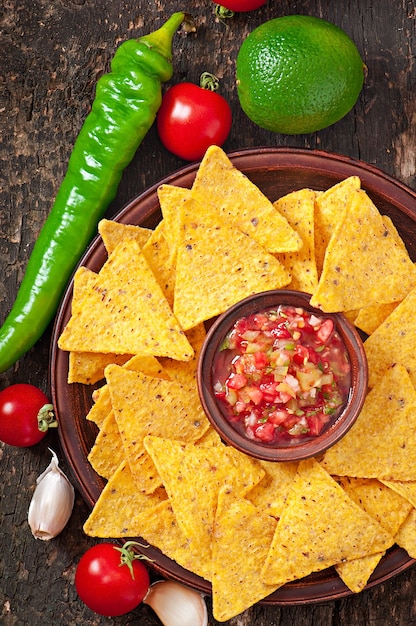 Mexican nacho chips and salsa dip in bowl on wooden